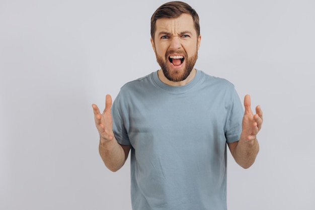 Retrato de un hombre moderno de mediana edad con barba en una camiseta azul que muestra emoción de ira y gritos en un fondo blanco