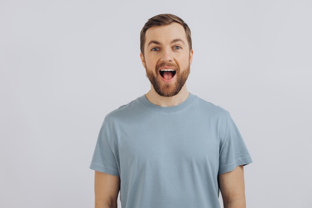 Retrato de un hombre moderno de mediana edad con barba en una camiseta azul que muestra emociones en un fondo blanco