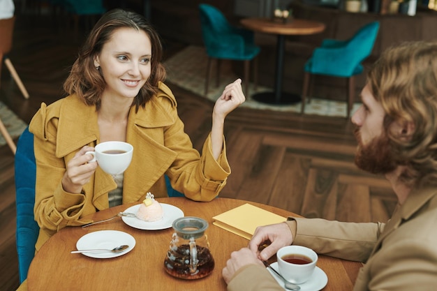 Retrato de un hombre moderno serio con barba sentado en una mesa redonda en un café loft y llamando por teléfono móvil