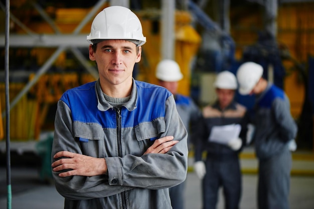 Retrato de un hombre con un mono y casco en el fondo de un grupo de trabajadores en la construcción de una fábrica