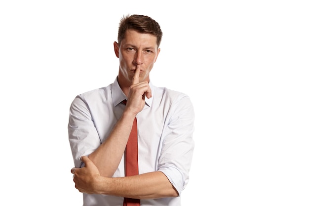 Retrato de un hombre moreno guapo con ojos marrones, vestido con una camisa blanca y una corbata roja. Él está mostrando una señal tranquila mientras posa en un estudio aislado sobre un fondo blanco. concepto de gesticul