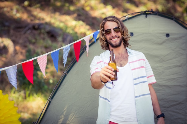 Retrato de hombre mostrando una botella de cerveza en el camping