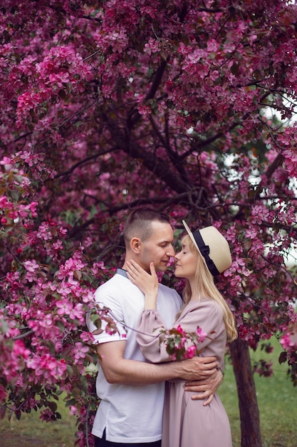 Retrato de hombre y mujer enamorados junto a un floreciente cerezo rosa en verano