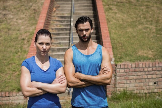 Retrato de hombre y mujer en forma de pie con los brazos cruzados contra la escalera en el campo de entrenamiento