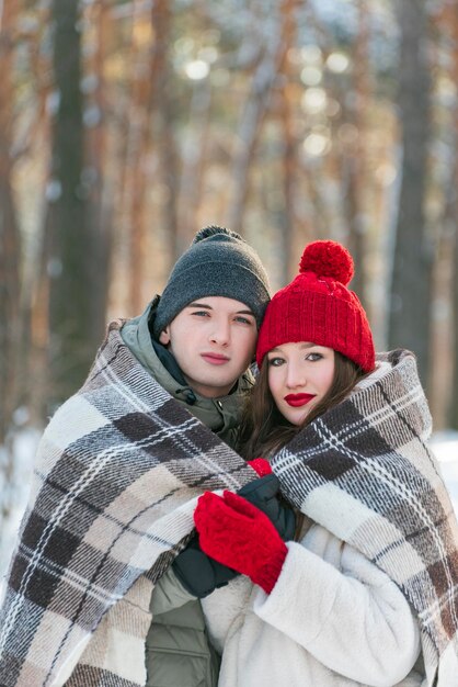 Retrato de un hombre y una mujer jóvenes en un bosque nevado de invierno se cubrieron con una manta cálida Marco vertical