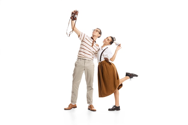 Retrato de hombre y mujer posando tomando selfie con cámara vintage aislado sobre fondo blanco.