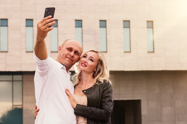 Retrato de un hombre y una mujer sonriendo mientras toma selfie en la ciudad