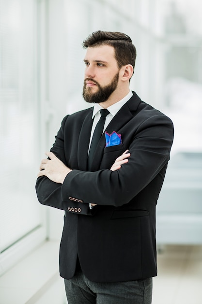 Retrato de hombre de negocios acertado de pie cerca de una ventana en la oficina brillante.