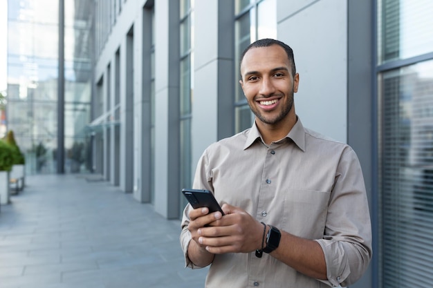 Retrato de un hombre de negocios afroamericano sosteniendo un teléfono sonriendo y mirando la oficina de la cámara