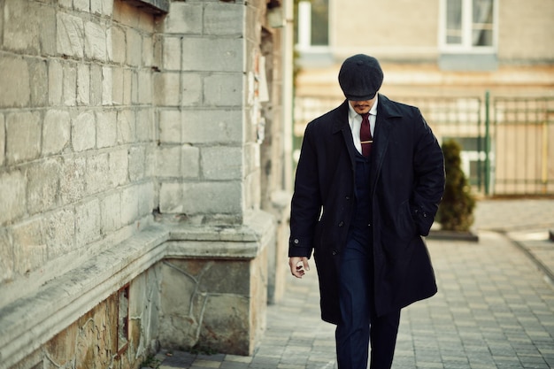 Retrato de un hombre de negocios árabe inglés de la década de 1920 con abrigo oscuro, traje, corbata y gorra plana