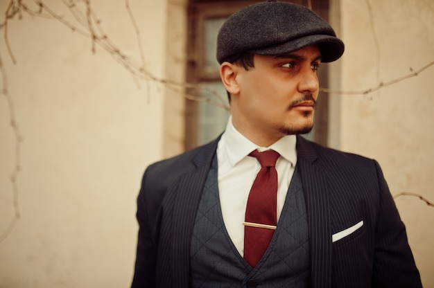 Retrato de hombre de negocios árabe inglés retro de los años 20 con traje oscuro, corbata y gorra plana.