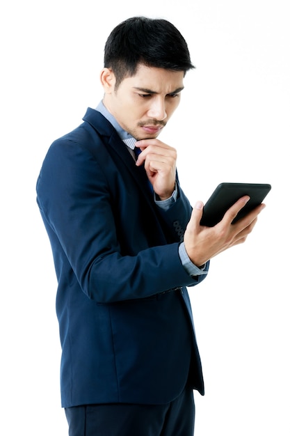 Retrato de hombre de negocios asiático joven serio en pose de pensamiento mientras comprueba la estrategia de la empresa en tableta sobre fondo blanco aislado. Estudio de disparo, concepto de planificación empresarial.