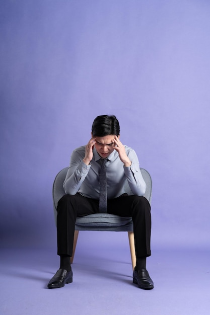 Foto retrato de un hombre de negocios asiático sentado en un sofá aislado sobre un fondo púrpura