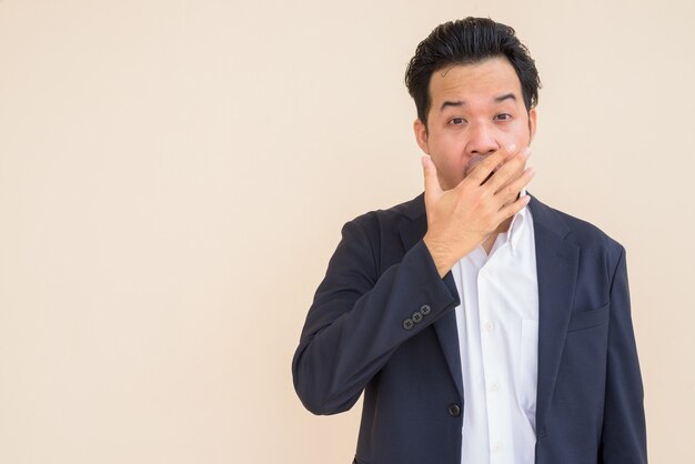 Retrato de hombre de negocios asiático vistiendo traje contra el fondo liso mientras mira conmocionado