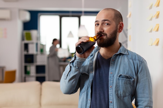 Retrato de un hombre de negocios bebiendo cerveza alcohólica de una botella, disfrutando de la celebración con bebidas después de las horas de trabajo. Trabajador feliz reuniéndose con colegas en la oficina para divertirse con alcohol y bocadillos.