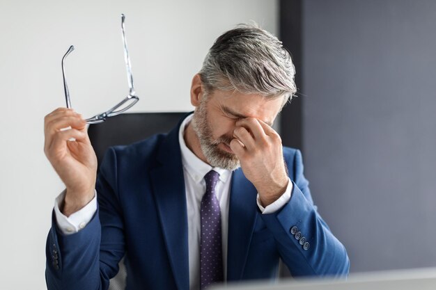 Retrato de un hombre de negocios cansado de mediana edad que sufre fatiga ocular en el lugar de trabajo