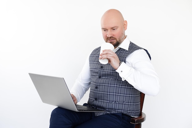 Retrato de hombre de negocios en chaleco gris blue jeans camisa blanca sosteniendo portátil blanco taza de café para llevar bebiendo