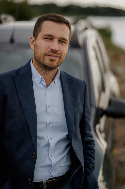 Retrato de hombre de negocios con coche clásico negro con traje negro. El hombre está parado cerca de su coche al aire libre.