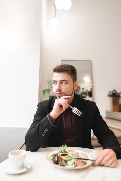 Retrato de un hombre de negocios comiendo una ensalada apetitosa en un acogedor restaurante ligero y mirando por la ventana