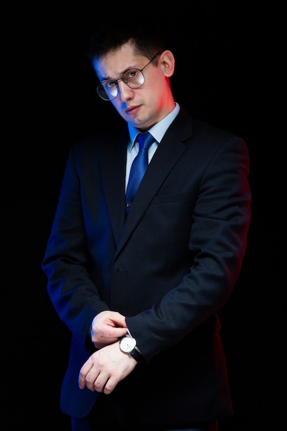 Retrato de hombre de negocios elegante guapo confiado en gafas con la mano en su traje sobre fondo negro