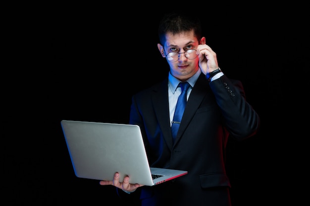 Retrato de hombre de negocios elegante guapo confiado con laptop en sus manos sobre fondo negro