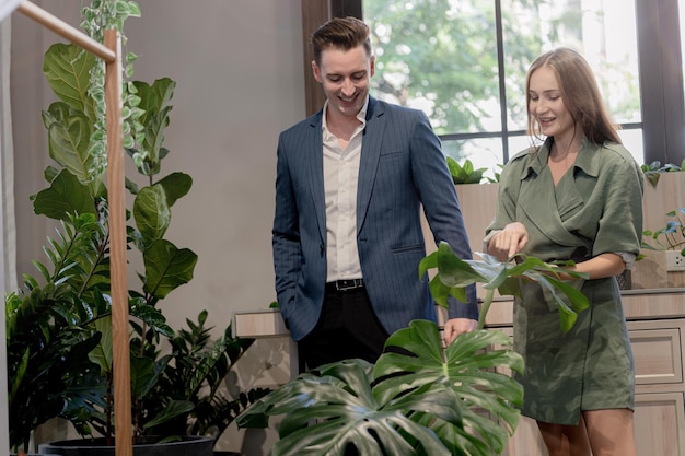 Retrato de un hombre de negocios feliz y una mujer revisan y tratan las hojas de las plantas de los árboles verdes en el jardín interior del edificio Concepto de espacio de oficina con naturaleza de biofilia