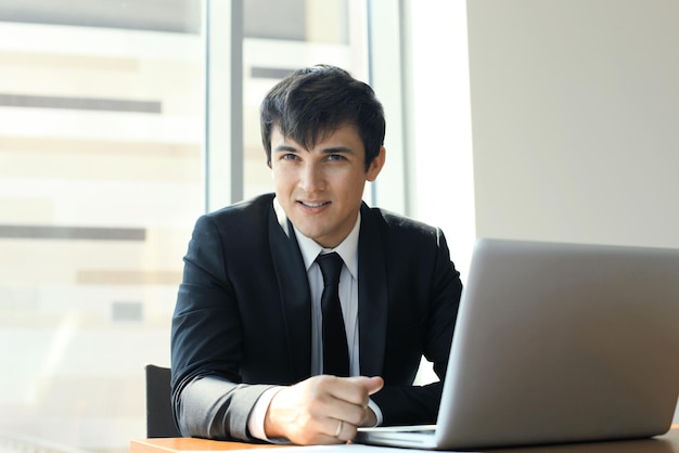 Retrato de hombre de negocios feliz sentado en el escritorio de oficina, mirando a cámara, sonriendo.