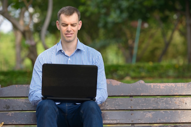 Retrato de hombre de negocios feliz usando laptop en el parque