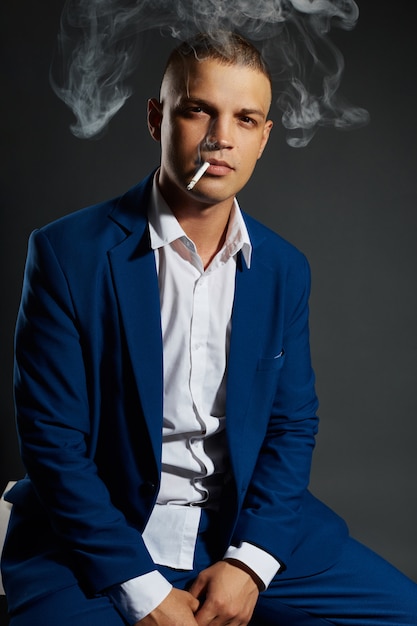 Retrato de un hombre de negocios fumador en un costoso traje de negocios sobre un fondo oscuro
