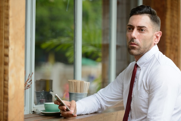 Retrato de hombre de negocios guapo con barba incipiente relajándose en la cafetería al aire libre