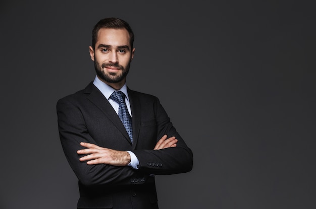 Retrato de un hombre de negocios guapo confiado vistiendo traje aislado, brazos cruzados