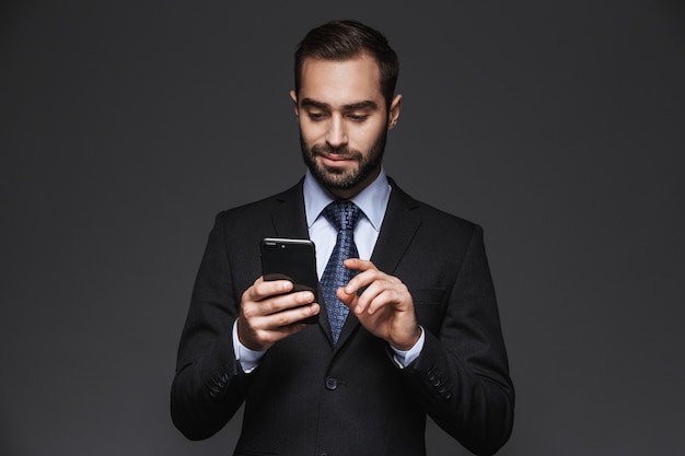 Retrato de un hombre de negocios guapo confiado vistiendo traje aislado, mediante teléfono móvil