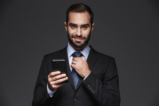 Retrato de un hombre de negocios guapo confiado vistiendo traje aislado, mediante teléfono móvil