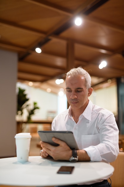 Retrato de hombre de negocios guapo sentado en la cafetería y con tableta digital