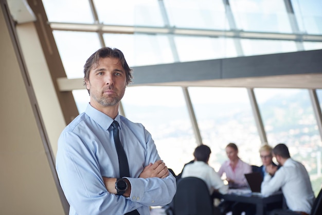 Foto retrato de hombre de negocios de handosme en una oficina moderna y luminosa en el interior con su equipo en grupo trabajando juntos en segundo plano