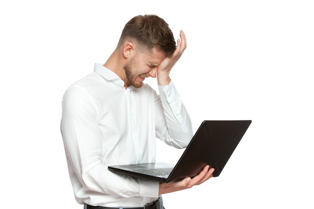 El retrato de un hombre de negocios joven con una computadora portátil en sus manos expresa la emoción de la desesperación y los gestos en una camisa blanca aislada en un fondo blanco.