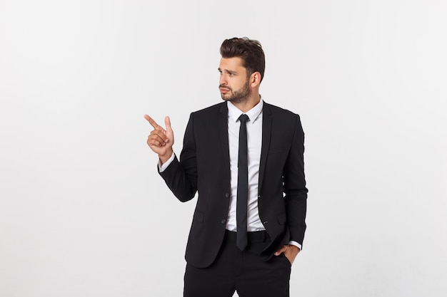 Retrato del hombre de negocios joven en traje que señala en el espacio de la copia sobre blanco.