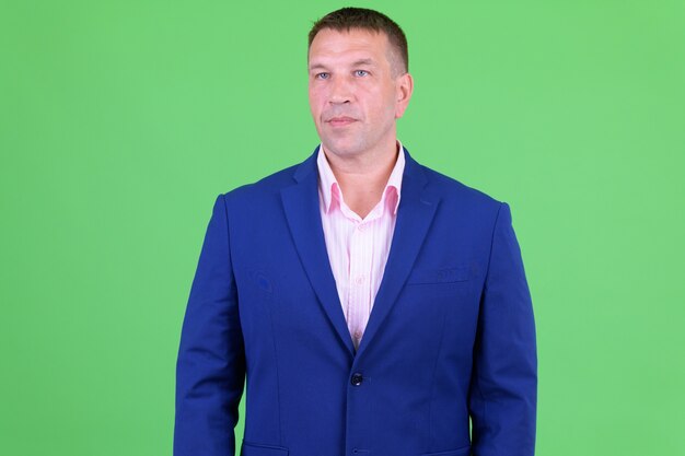 Retrato de hombre de negocios macho maduro vistiendo traje azul contra chroma key con pared verde