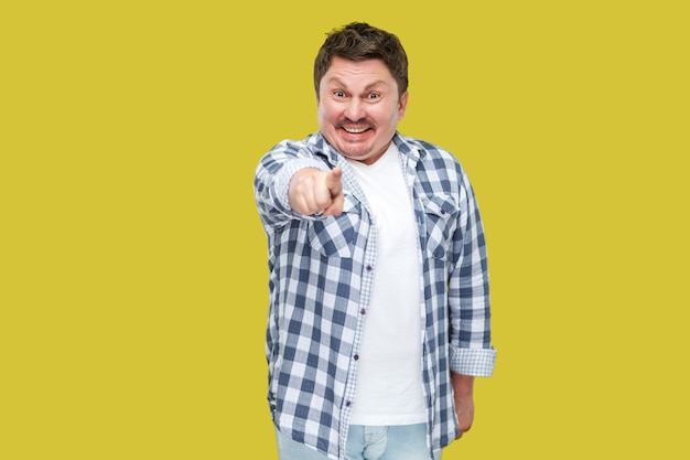 Retrato de hombre de negocios de mediana edad guapo feliz emocionado en camisa a cuadros casual de pie, apuntando y mirando a cámara con una gran sonrisa. tiro del estudio de interior, aislado en fondo amarillo.