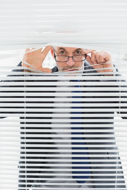 Retrato de un hombre de negocios mirando a través de las persianas en la oficina