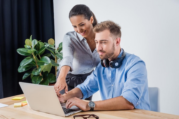 Retrato de un hombre de negocios que trabaja en una laptop con un colega sonriente en la oficina