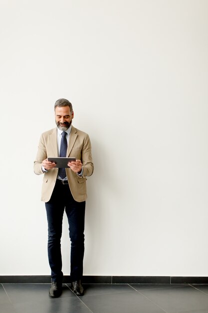 Retrato de hombre de negocios senior guapo con tableta por pared