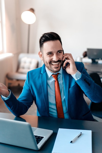 Retrato del hombre de negocios sonriente que habla en el teléfono móvil en oficina