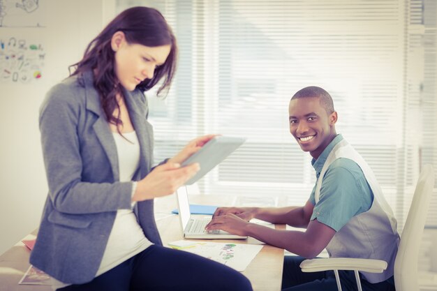 Foto retrato del hombre de negocios sonriente que trabaja en la computadora portátil con la mujer que usa la tableta digital