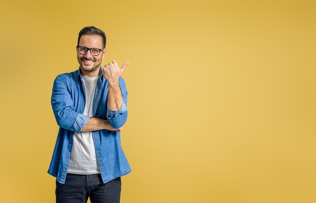 Retrato de un hombre de negocios sonriente señalando con el pulgar el espacio de copia para marketing sobre fondo amarillo