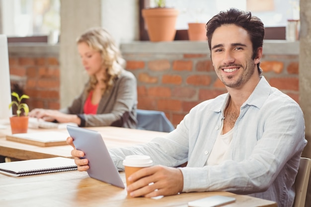 Retrato de hombre de negocios sonriente con tableta digital y café en la oficina