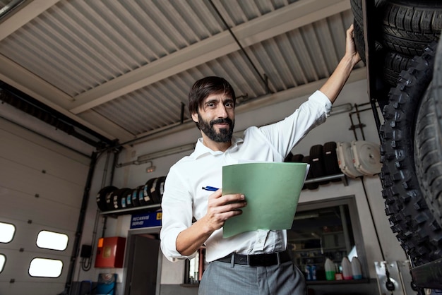 Retrato de un hombre de negocios sosteniendo un documento mientras está de pie con neumáticos en el garaje