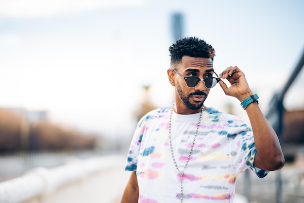 Retrato de un hombre negro con una camiseta colorida mirando sus gafas de sol