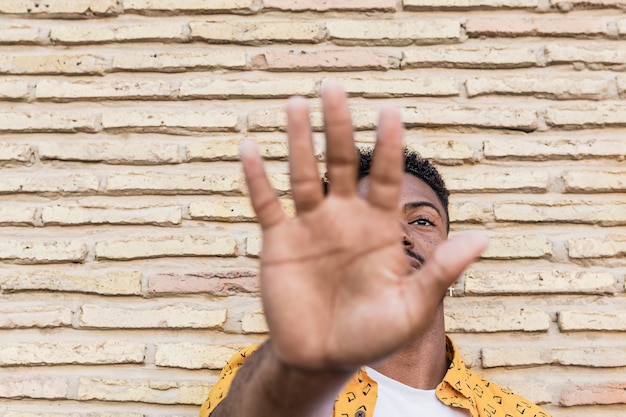 Retrato de un hombre negro guapo mostrando su palma haciendo señal de stop con un fondo de ladrillo