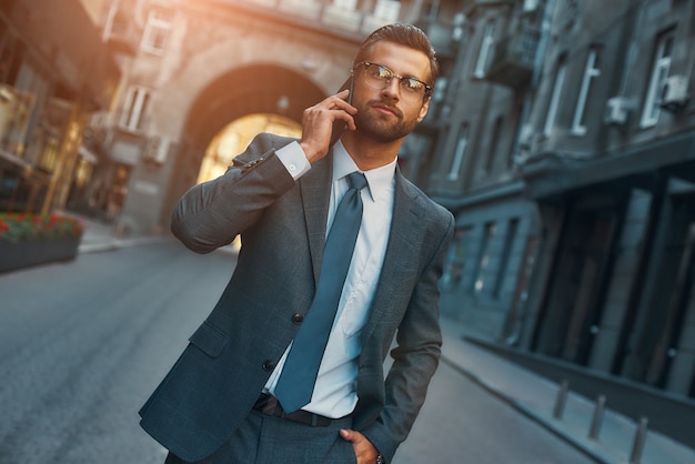 Retrato de hombre ocupado del empresario barbudo en traje completo hablando por teléfono con el cliente mientras